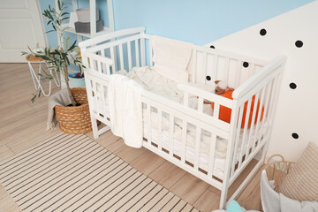 Stylish white crib with plaid and olive tree near blue wall in interior of children's room