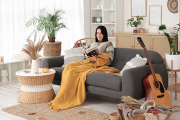 Young happy woman with warm plaid and magazine sitting on sofa at home
