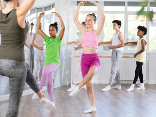 Teen girl in casual sportswear practicing ballet movements with focus and grace during group dance class session..