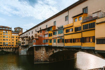 Ponte vecchio, the only bridge in florence spared from destruction during world war ii, houses shops built along it, reflecting on the arno river under a cloudy sky
