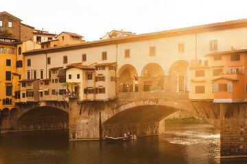 Obraz premium The historic ponte vecchio bridge in florence glows at sunset, reflecting on the arno river, creating a picturesque italian scene
