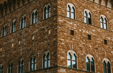 Sunlight illuminates the corner and facade of a building, showcasing its beautiful arched windows and intricate brickwork, a testament to florence's rich history and architectural prowess