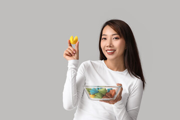 Young Asian woman with colorful fortune cookies on grey background
