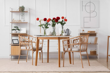 Vases with beautiful dahlia flowers and tea set on dining table at home