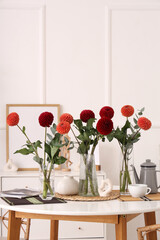 Vases with beautiful dahlia flowers and tea set on dining table at home