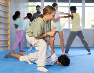 Focused teenage girl learning effective self defence techniques in sparring with boy, practicing...