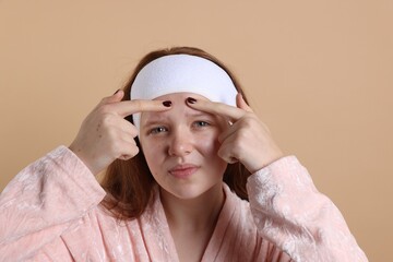 Teenage girl popping pimple on her face against beige background. Acne problem