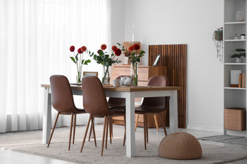 Vases with beautiful dahlia flowers and tea set on dining table at home