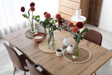 Vases with beautiful dahlia flowers and tea set on dining table at home