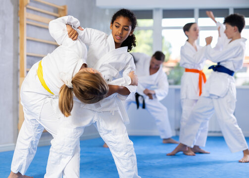 Two girls in kimonos train judo techniques in group in studio..