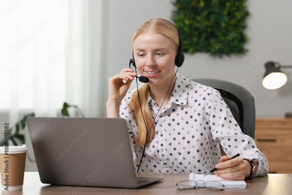 Poster interpreter in headset taking notes while working with laptop at table indoors