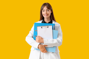 Beautiful businesswoman with folders and clipboard on yellow background