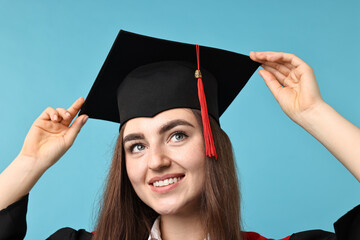 Happy student after graduation on light blue background