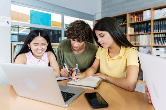 Three young multiracial group of high school students working together on laptop at library. Education and youth lifestyle concept.