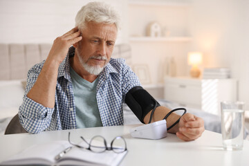 Senior man measuring blood pressure at table indoors