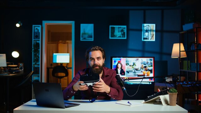 Technology specialist reviewing VR goggles in RGB lights lit studio. Professional media star filming technology channel vlog for gadget enthusiasts using camera and microphone