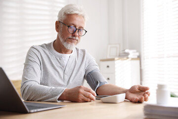 Senior man measuring blood pressure at table indoors