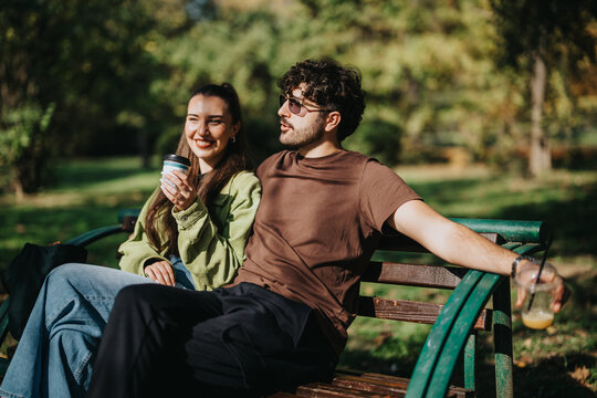 A cheerful couple sits on a park bench, savoring iced drinks and each others company on a sunny day. The scene captures relaxation and happiness in a lush green environment.