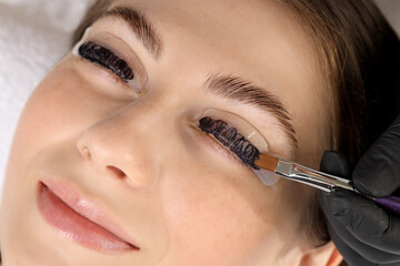 Eyelash lamination procedure. Esthetician applying dye on woman's eyelashes in beauty salon, closeup