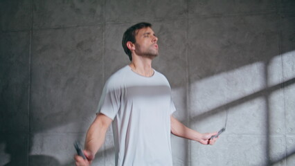 Athletic guy practicing fitness training with jumping rope at empty room closeup