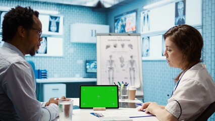 Physician specialist looking at chroma key display in medical office, doing a consultation with a diagnostic report. Medic consulting african american patient during checkup. Camera B.