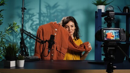 Influencer filming fashion content using professional camera, showing audience jacket purchase she recently did. Fashionista doing vlog, presenting viewers new clothing acquisition, camera B