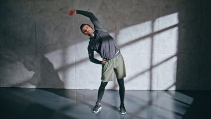 Athletic man preparing fitness workout in dark gym. Fitness guy stretching body