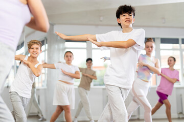 Team of positive teenagers rehearsing modern dances in dance hall