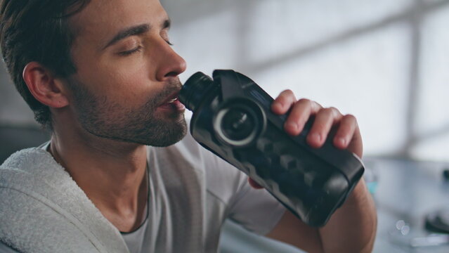 Muscular athlete drinking bottle at gym portrait. thirsty man looking camera