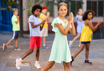 Cheerful tween girl street dancer posing during performance with group in summer city ..