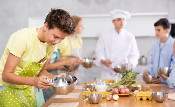 Cooking course - portrait of teenage boy in an apron who is learning to beat eggs to make pancakes at a cooking class