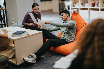 Obraz premium Students engaged in teamwork, sharing ideas on a project while seated in a modern school environment with a cozy bean bag chair, promoting creativity and collaboration.