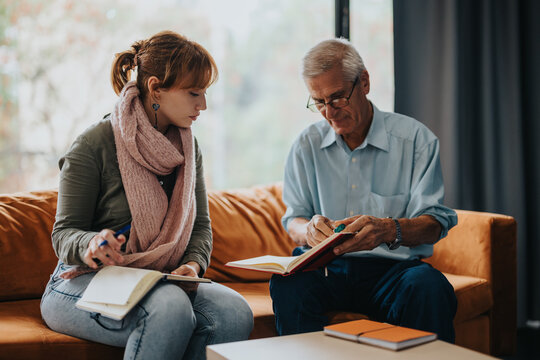 A senior professor assists a female student with her notes. They engage in a thoughtful discussion in a comfortable setting, showcasing mentorship and learning.