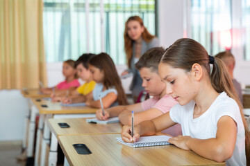 Pupils sitting in classroom during lesson. Female teacher standing behind.