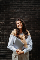 Young businesswoman holding laptop in front of black brick wall	