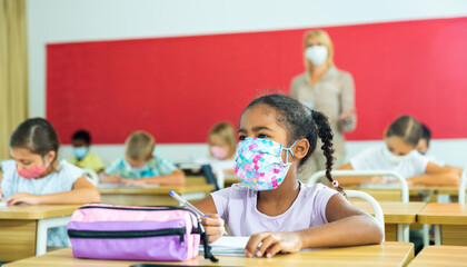 Primary school students in protective masks sit at school desk in the classroom