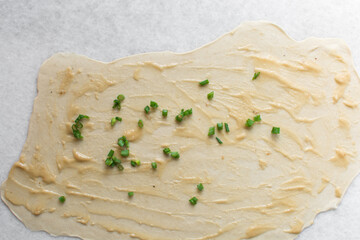 Overhead view of green scallions on oiled pancake dough, top view of sliced green onion on rolled out scallion pancake dough, process of making flaky scallion pancake
