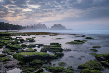 the beautiful view of a tropical beach in the morning, with white sand and coral rocks hit by ocean waves. Landscape images are taken with slow speed technique.
