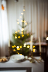 Long beige white candles in a candlestick with brown velvet bows. Christmas trees and fir tree branches on a white wooden table