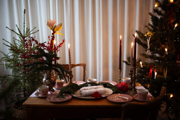 Traditional Christmas stollen fruit cake on festive laying table, preparation for christmas dinner with candles. Christmas tree and fir tree branches on a brown wooden table