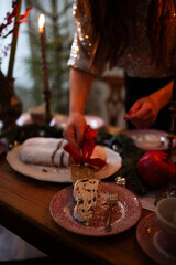 A girl is setting a beautifully arranged dining table with candles, festive decorations, and greenery, creating a warm atmosphere for a holiday celebration.