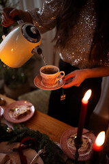 Close up of a woman hand pouring black tea from a teapot into a cup on a near festive laying table, preparation for christmas dinner.