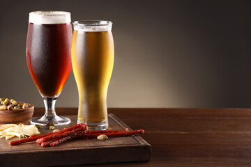 Glasses with different types of beer and snacks on wooden table, closeup. Space for text