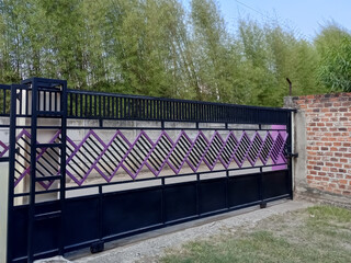 A modern, minimalist sliding gate with a black frame and purple accents in front of a green bamboo...