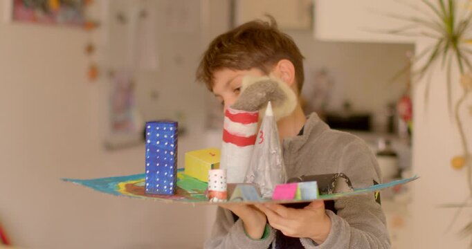 A young boy excitedly presents his imaginative and creative model of a vibrant miniature city that has been joyfully crafted from various recycled materials, showcasing his skills and creativity