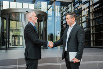 experienced senior executive warmly greeting younger business partner with confident handshake...