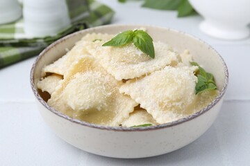 Delicious ravioli with cheese and basil on white tiled table, closeup