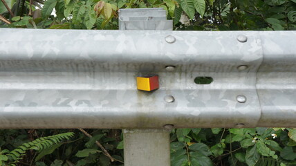 Small Cube on Metal Road Barrier in Lush Green Foliage