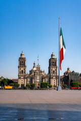 Mexico City Metropolitan Cathedral with a Large Mexican Flag in Zocalo Square, Showcasing Historic Architecture and National Symbolism Under a Clear Blue Sky on a Sunny Morning