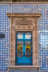 Naklejka premium A close-up of a window in Casa de los Azulejos, featuring intricate blue and white tiles, a decorative stone frame, and wrought iron details.
